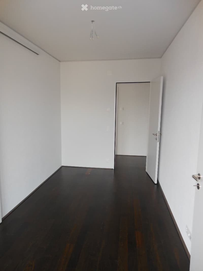 Empty room with white walls, dark wooden floor, and a single open door leading to another space.