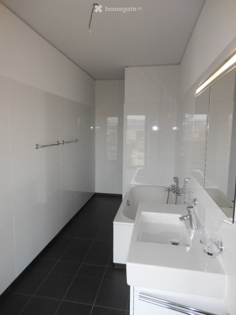 Modern bathroom with white tiles, black floor, double sink, bathtub, and large mirror.