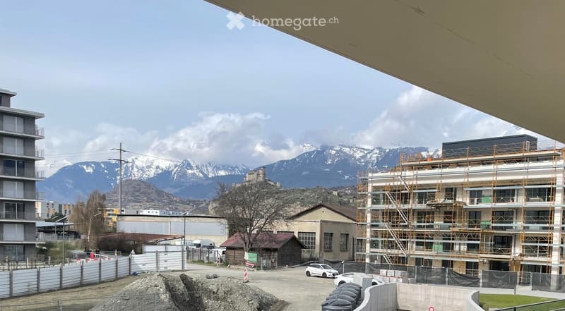 View of a construction site with a partially built multi-story building, scaffolding, and a mountainous backdrop.