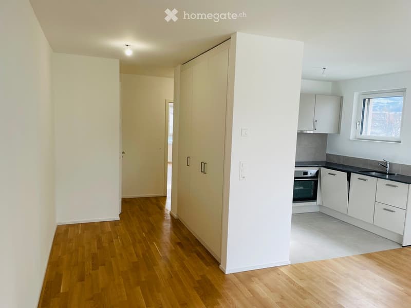 Modern, unfurnished room with wooden flooring, white cabinets, and a small kitchen area featuring an oven, sink, and faucet.