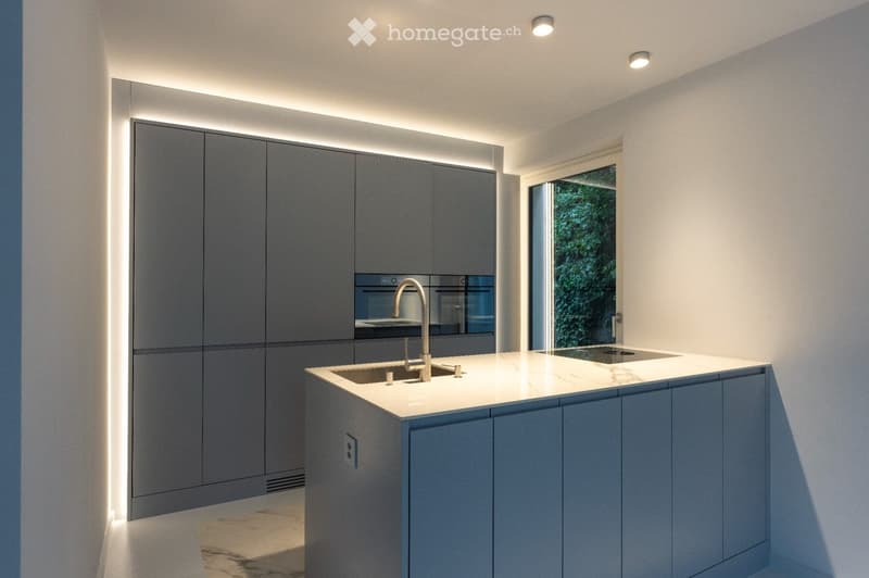 Modern kitchen with grey cabinets, white countertop, built-in oven, and sleek faucet.