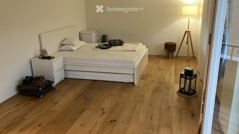 Modern bedroom with a white bed, nightstand, floor lamp, small stool, and decorative lantern on the floor.