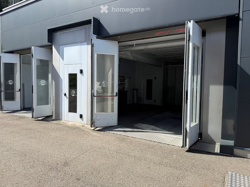 Exterior view of a modern building with multiple open doors and glass panels, featuring a clean and organized entrance area.