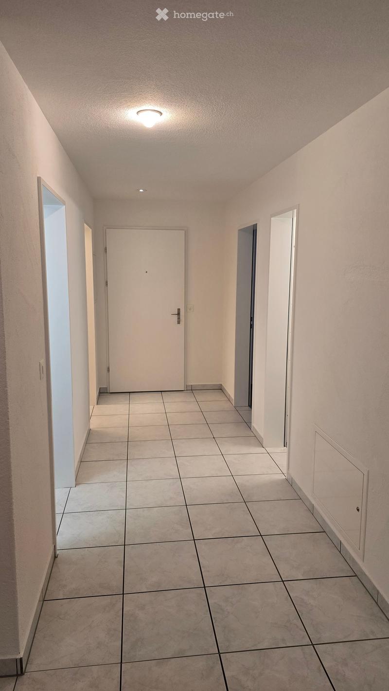 Empty hallway with tiled floor, white walls, and several doors leading to other rooms.