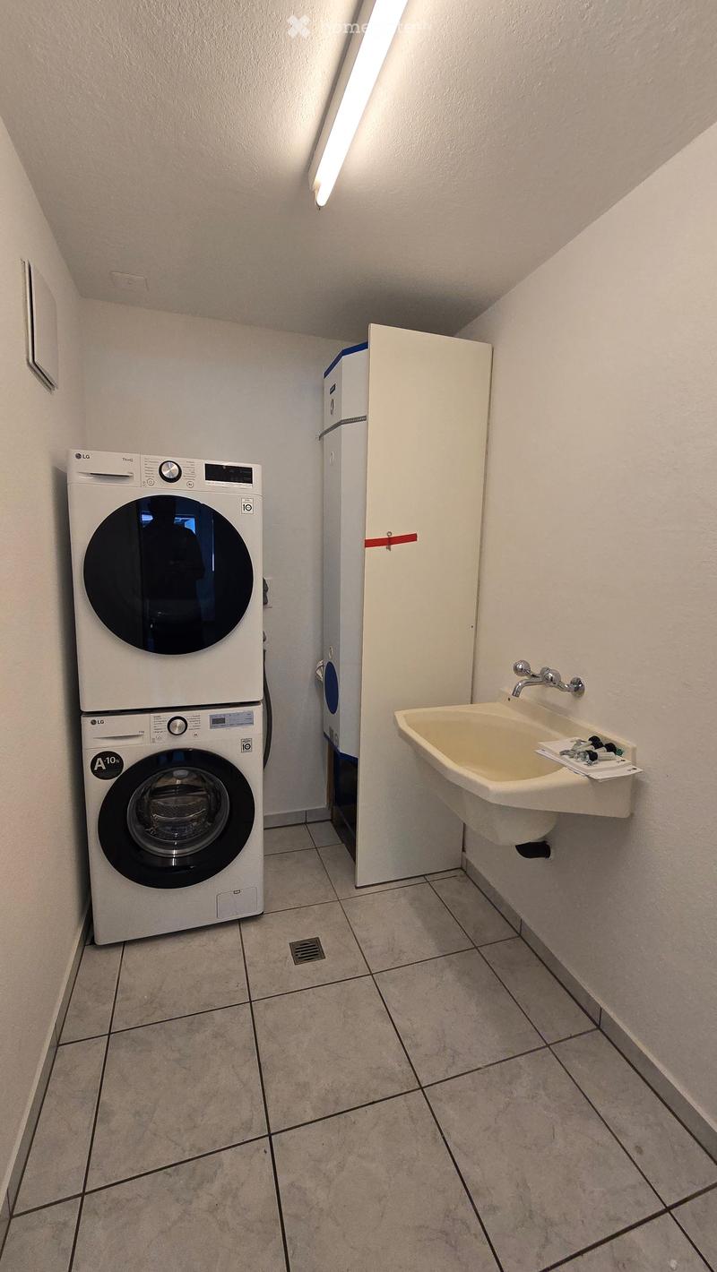 Bathroom with a washing machine, sink, and tiled floor.