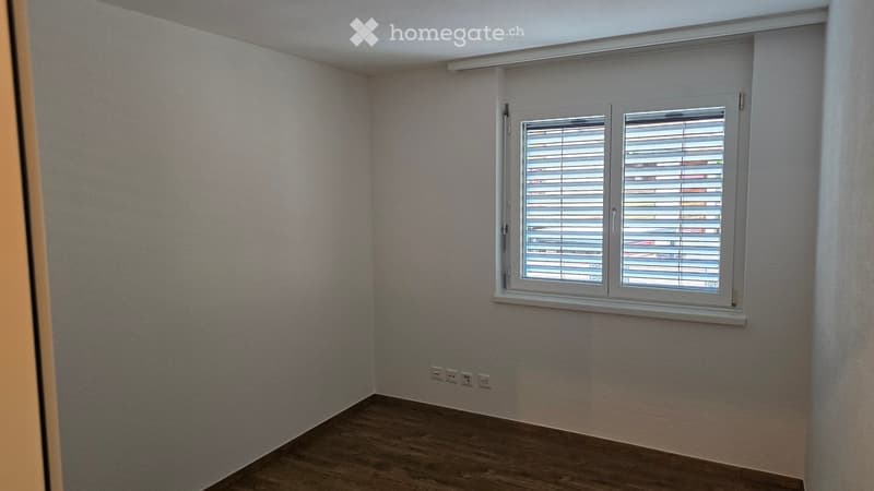 Empty room with light-colored walls, wooden flooring, and a window with blinds. No furniture or equipment is present.