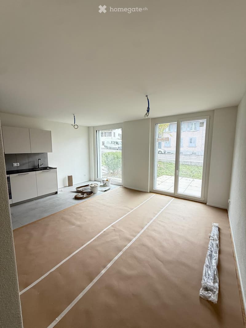 Empty room with unfinished flooring, white cabinets, and large windows with sliding doors leading to a patio.