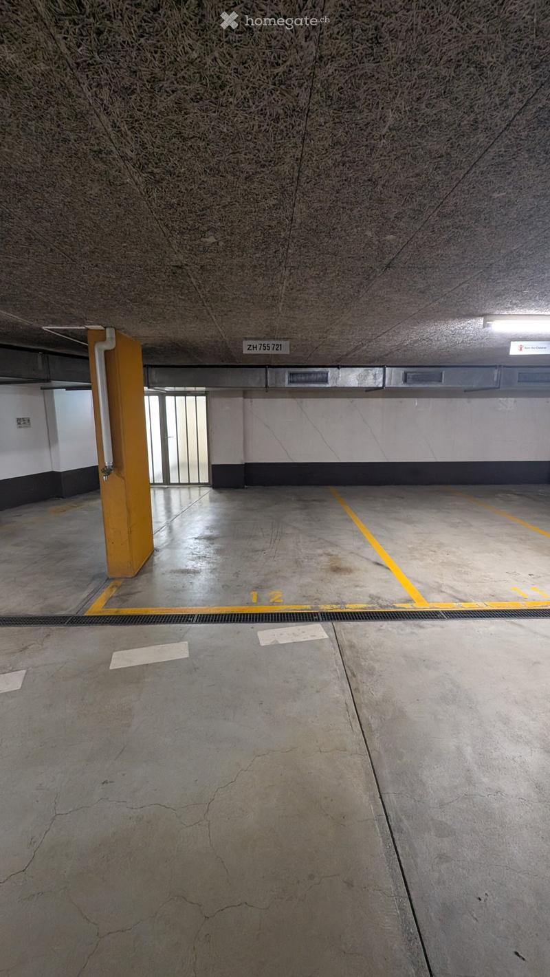 Underground parking area with concrete floors, yellow parking lines, and a single pillar. The area is empty with no vehicles present.