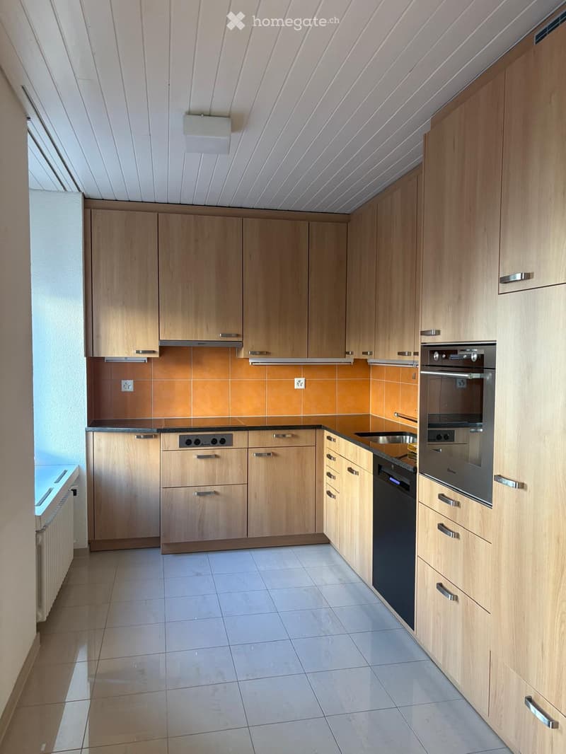 Modern kitchen with light wooden cabinets, stainless steel appliances, and a tiled backsplash.