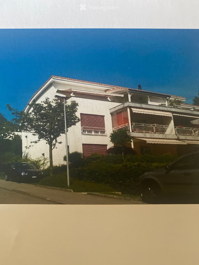 Two-story white house with red shutters, balcony, and garage. Two cars parked in front.