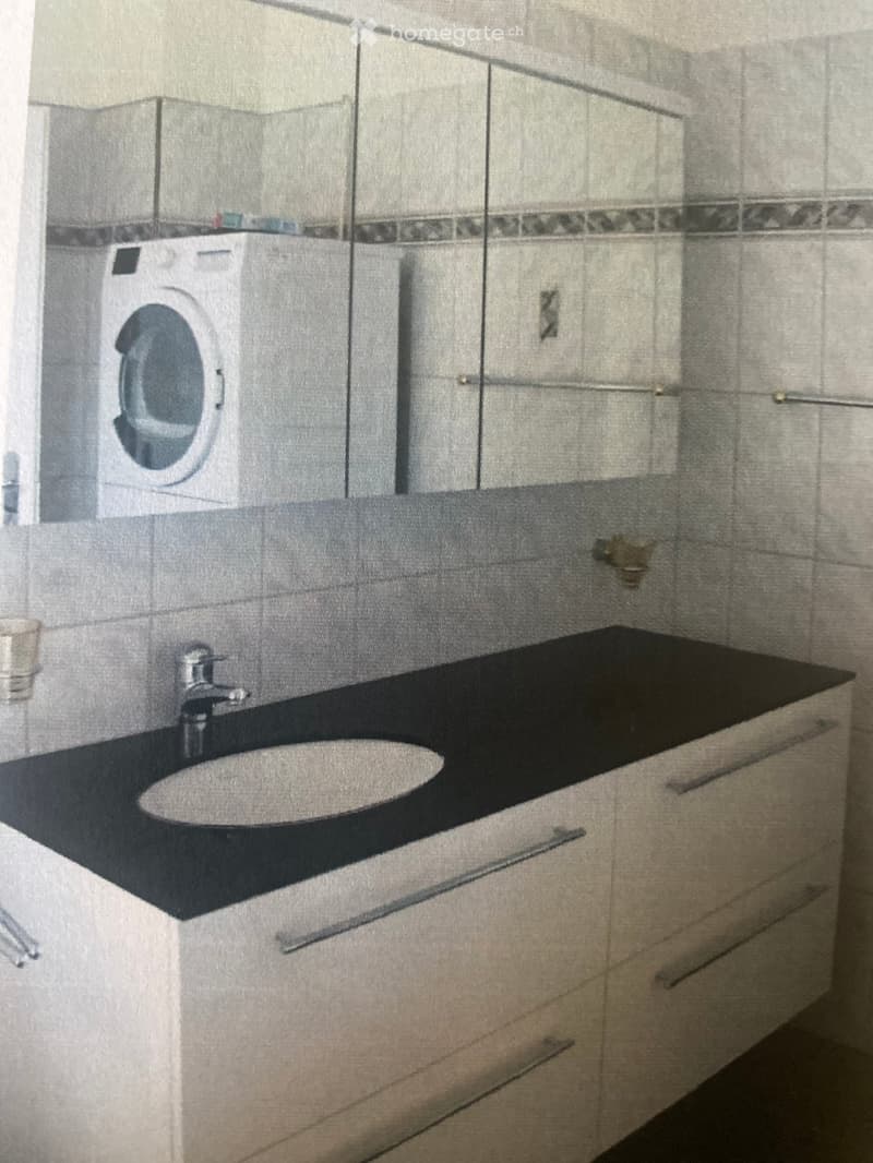Modern bathroom with a black countertop sink, chrome faucet, and a washing machine in the background.
