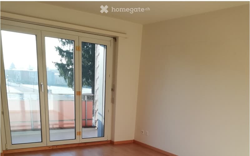 Empty room with wooden flooring, white walls, and large glass sliding doors leading to a balcony or outdoor area.