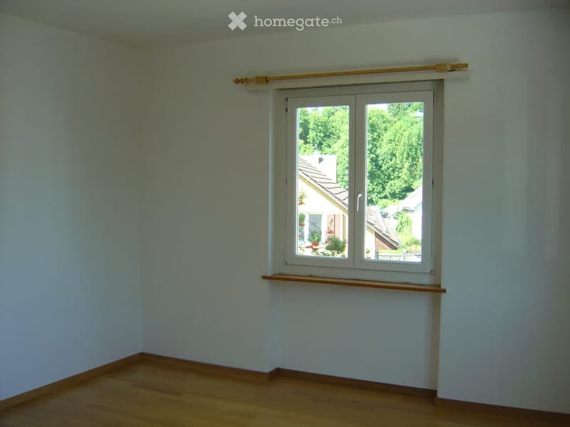 Empty room with light-colored walls, wooden flooring, and a large window with a wooden sill and blinds.