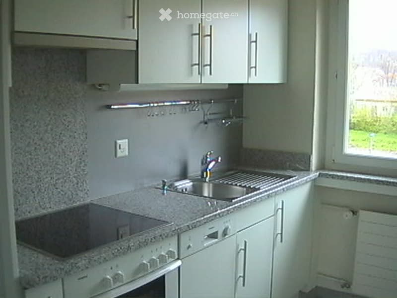 Modern kitchen with white cabinets, granite countertop, built-in stove, sink, and window overlooking a green area.