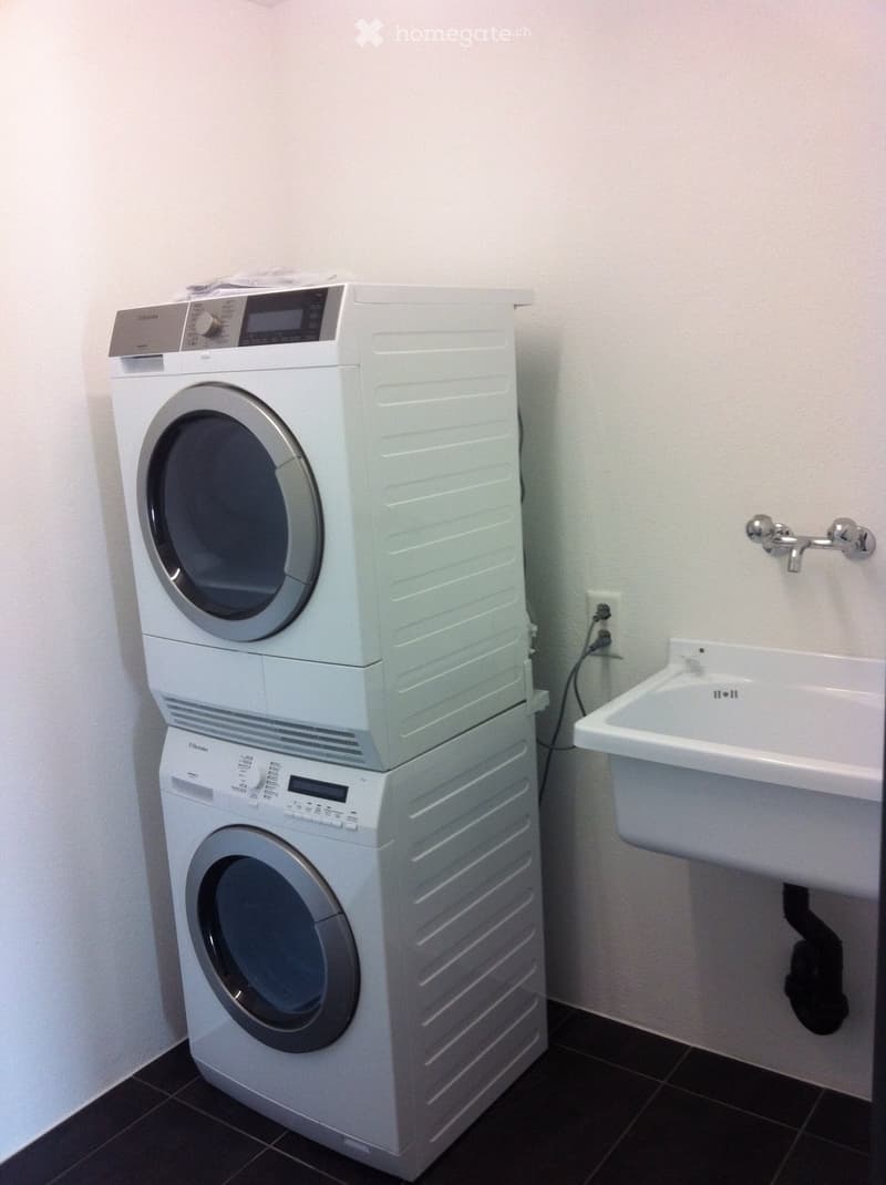 Bathroom with a stacked washing machine and dryer unit, a white sink with a faucet, and a tiled floor.