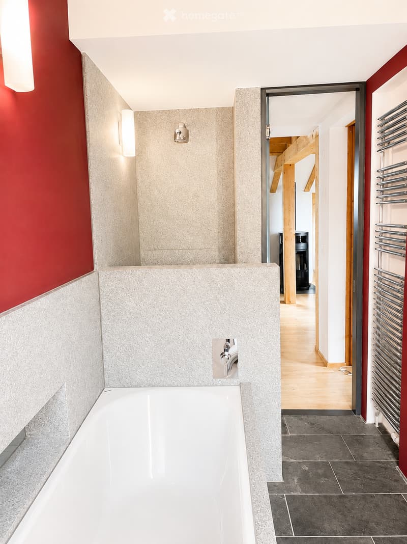 Modern bathroom with a large bathtub, sleek faucet, and a radiator on the wall. The space features textured tiles and a red accent wall.