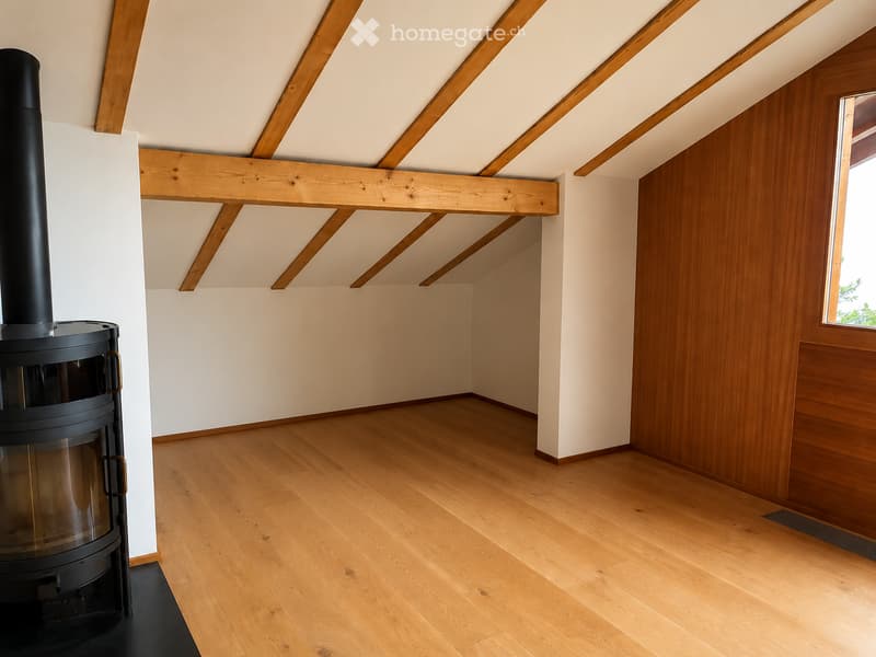Empty room with wooden floor, exposed wooden beams, white walls, and a black wood-burning stove with a chimney.