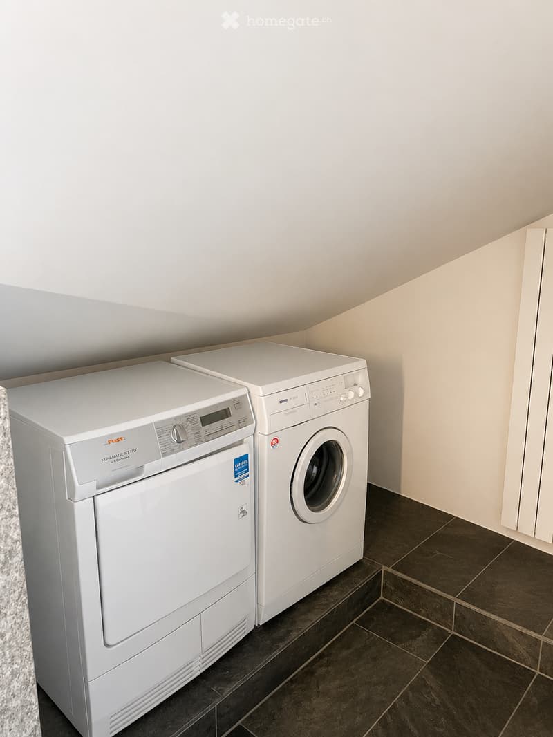 A small, well-lit room with a washing machine and dryer placed side by side on a dark tiled floor.