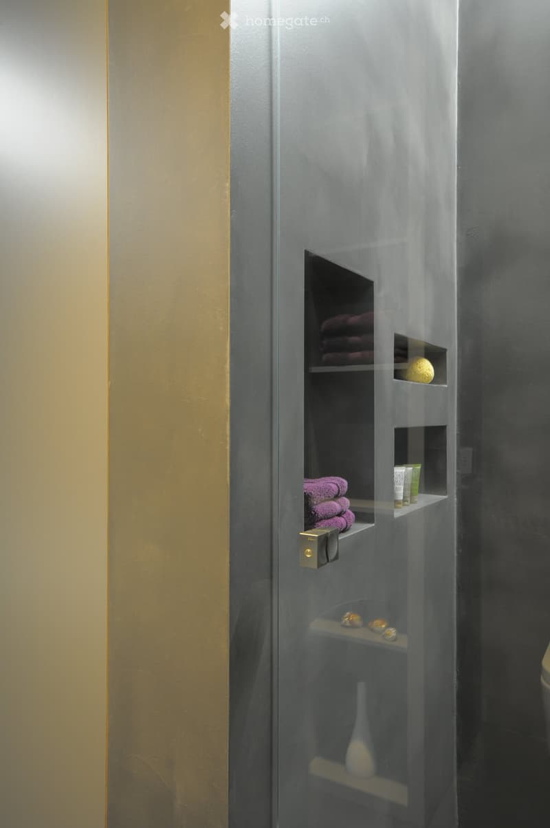 Modern bathroom with a glass shower enclosure, neatly stacked purple towels, decorative items, and a sleek design.