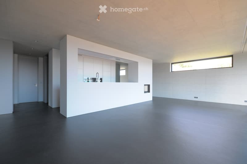 Modern, minimalist room with white walls, dark grey flooring, and a built-in kitchen counter with a sink and faucet. The space is open and uncluttered, with large windows providing natural light.