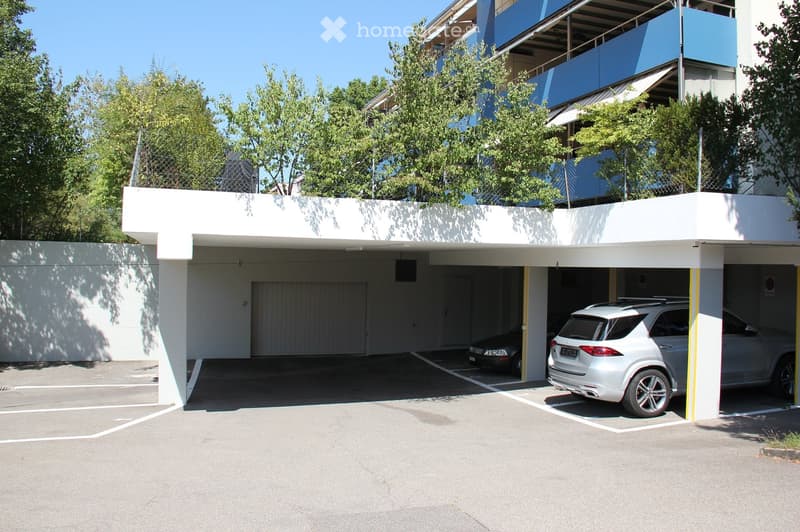 Modern multi-story building with a covered parking area, featuring two parked cars and a clean, organized space.