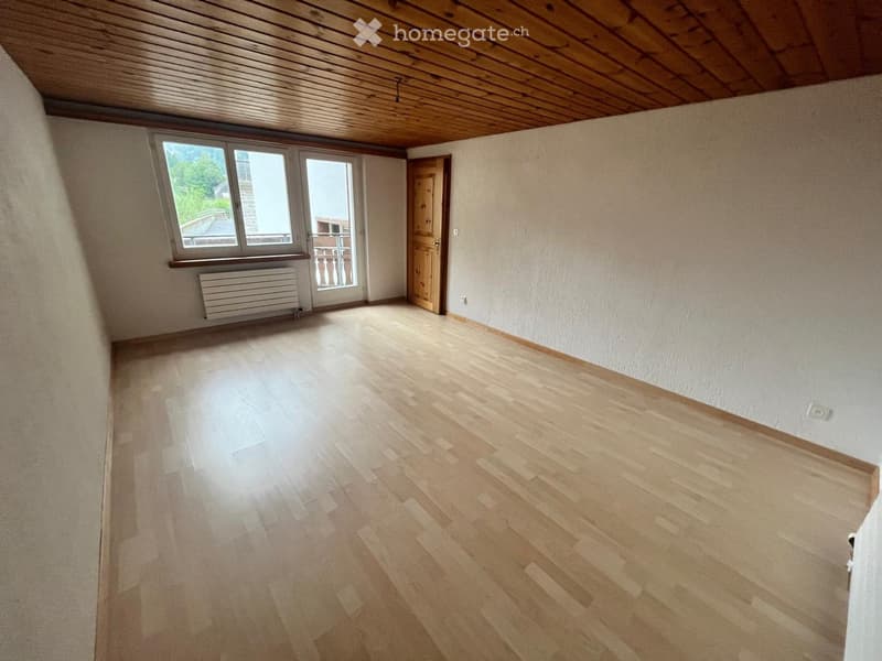 Empty room with wooden flooring, white walls, large window, and a door leading to a balcony.