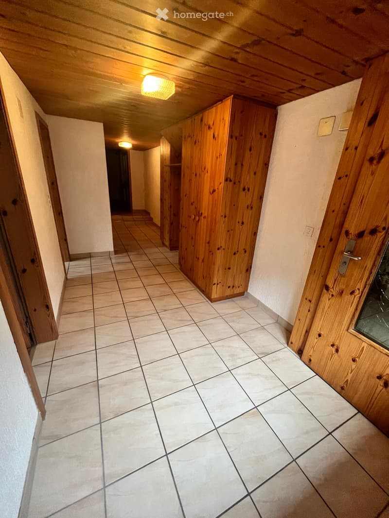 A narrow hallway with tiled flooring, wooden doors, and built-in wooden cabinets. The ceiling has exposed wooden beams and recessed lighting.