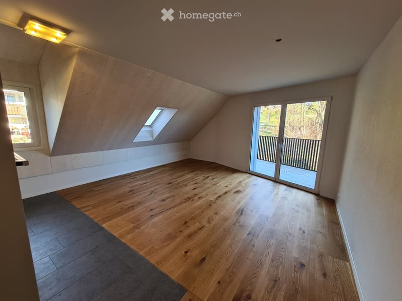 Empty attic room with wooden flooring, skylight windows, and a sliding glass door leading to a balcony.