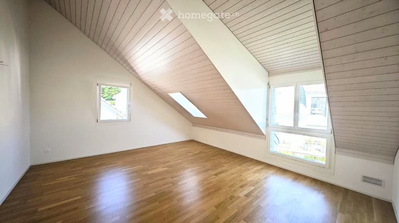 Empty attic room with wooden flooring, white walls, and multiple windows including a skylight, allowing natural light to fill the space.