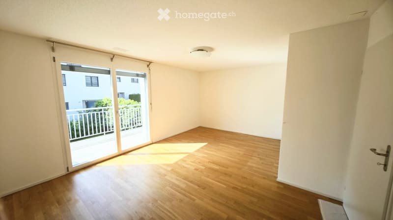 Empty room with wooden flooring, white walls, and a large sliding glass door leading to a balcony.