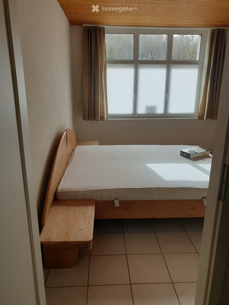 Cozy bedroom with a built-in wooden bed and bench, tiled floor, and large windows with blinds and curtains.