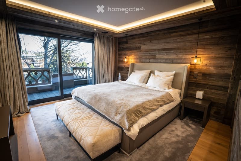 Modern bedroom with wooden walls, large bed, nightstand, bench, and balcony access.