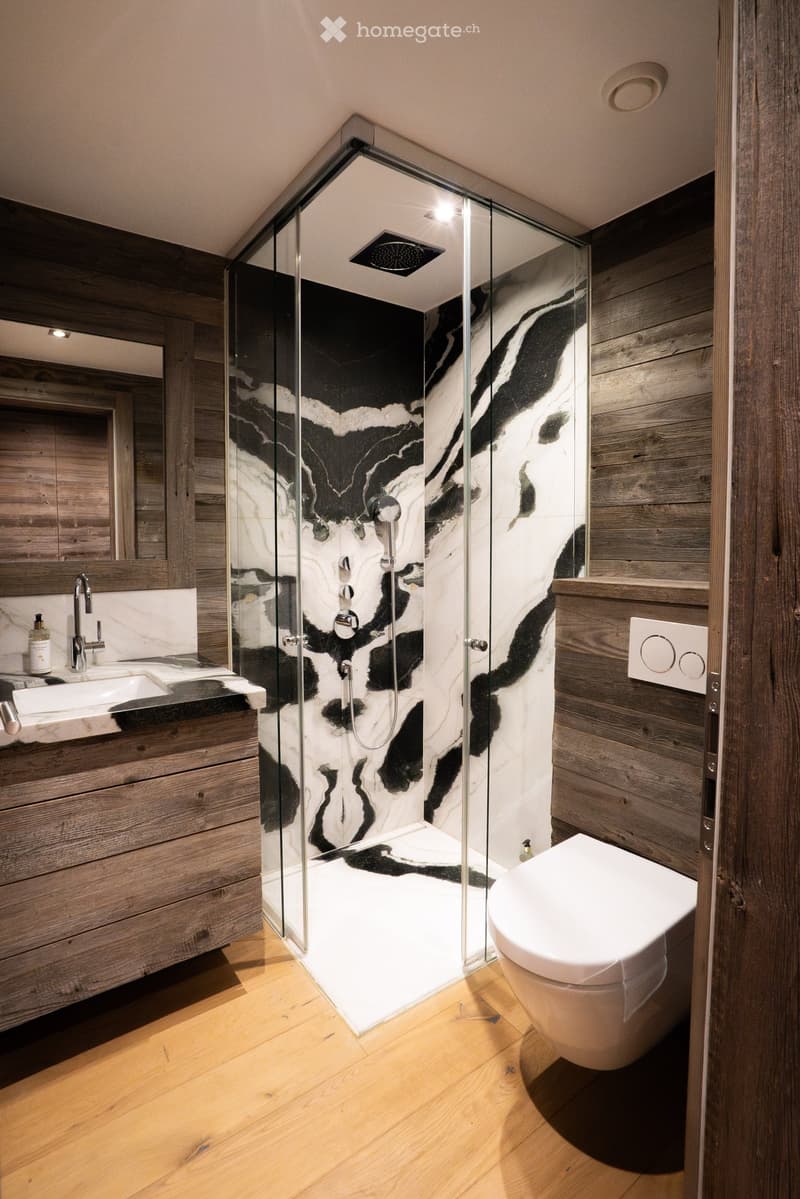 Modern bathroom with wooden walls, a glass-enclosed shower with black and white marble tiles, a white toilet, a sink with a chrome faucet, and a mirror above the sink.