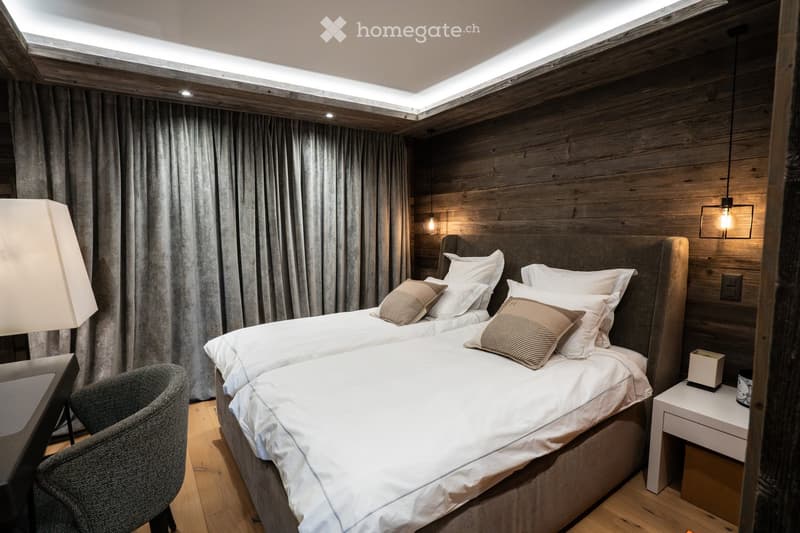 Modern bedroom with two double beds, wooden walls, large windows with curtains, a side table, and a chair.