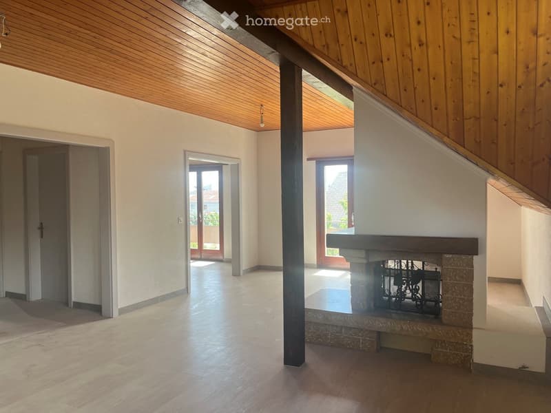 Empty room with wooden ceiling, light-colored walls, polished wooden floor, and a fireplace with a decorative metal screen. Two large windows and a door lead to an outdoor area.