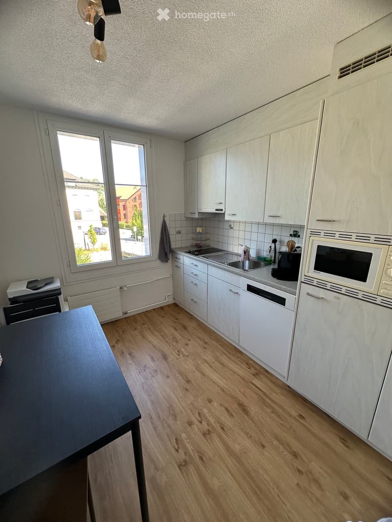 Modern kitchen with white cabinets, wooden flooring, a microwave, sink, and a table.