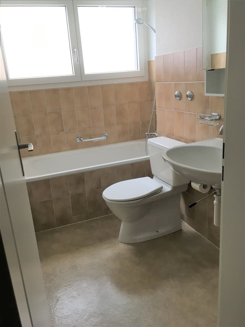 Bathroom with beige tiled walls, a bathtub, toilet, sink, and a window above the bathtub.