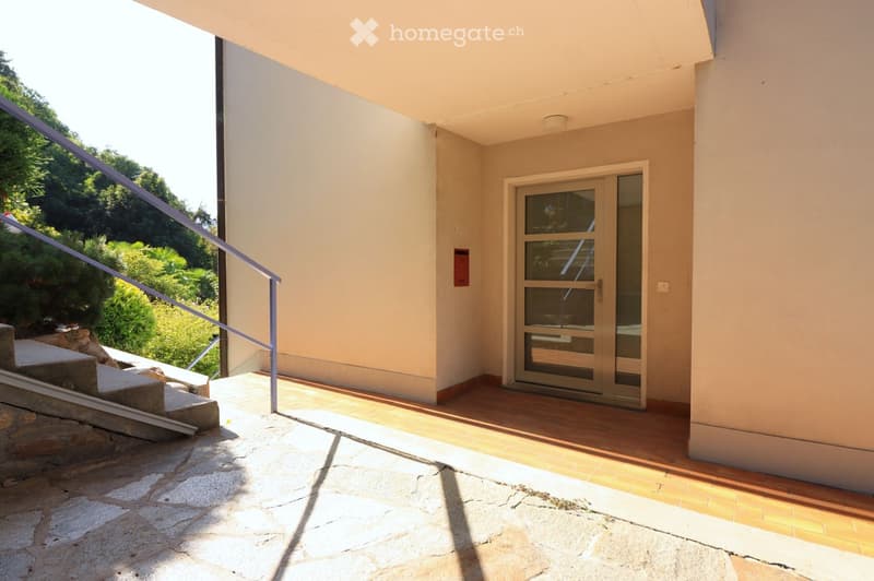 Balcony with wooden flooring, glass door, metal railing, and steps leading to a stone-paved area.