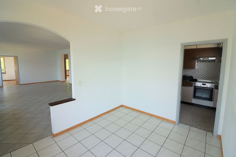 Empty room with tiled flooring and white walls, featuring an open doorway leading to another space and a small kitchen area with built-in appliances.