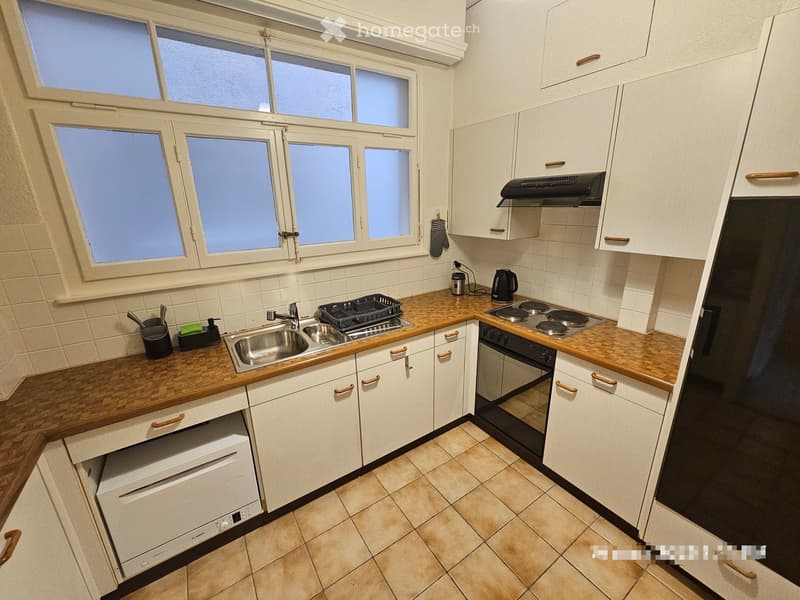 Modern kitchen with white cabinets, wooden countertops, stainless steel sink, stove, oven, and dishwasher. Features a window with multiple panes and tiled backsplash.