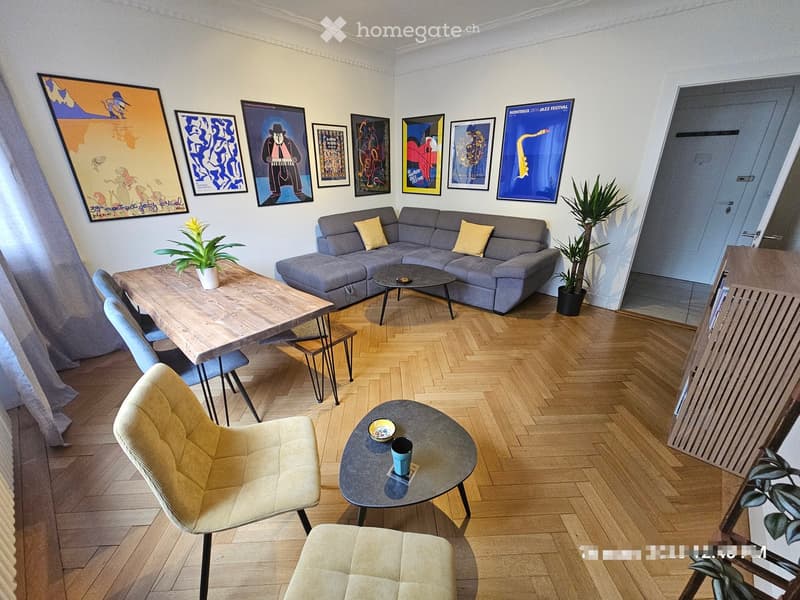 Modern living room with grey sectional sofa, wooden coffee table, small round side tables, and decorative artwork on the walls.