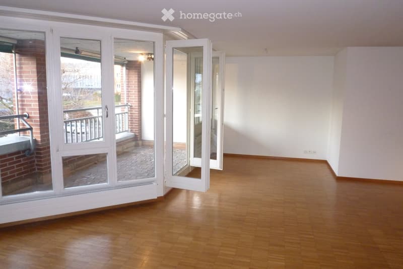 Empty room with wooden flooring and white walls, featuring large sliding glass doors that open to a balcony area.