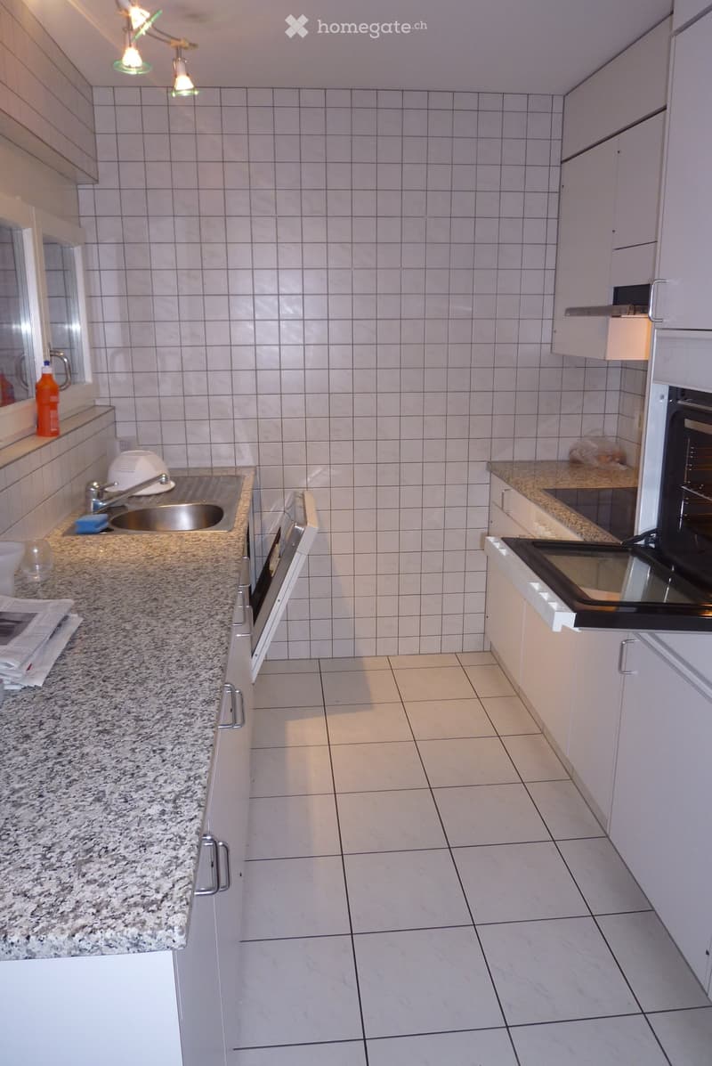 Modern kitchen with white tiled walls, granite countertops, and white cabinets. Features a sink, faucet, and built-in oven.