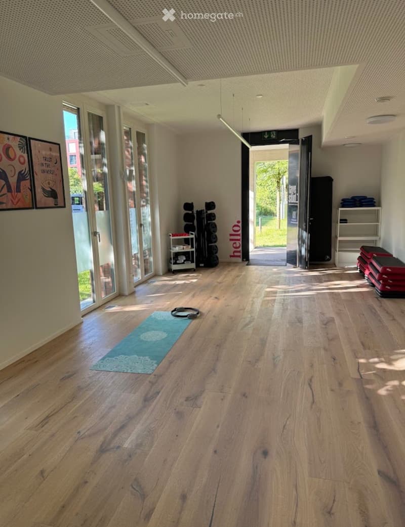 Bright, open space with wooden flooring, yoga mat, headphones, shelves, and a stack of mats near the entrance.