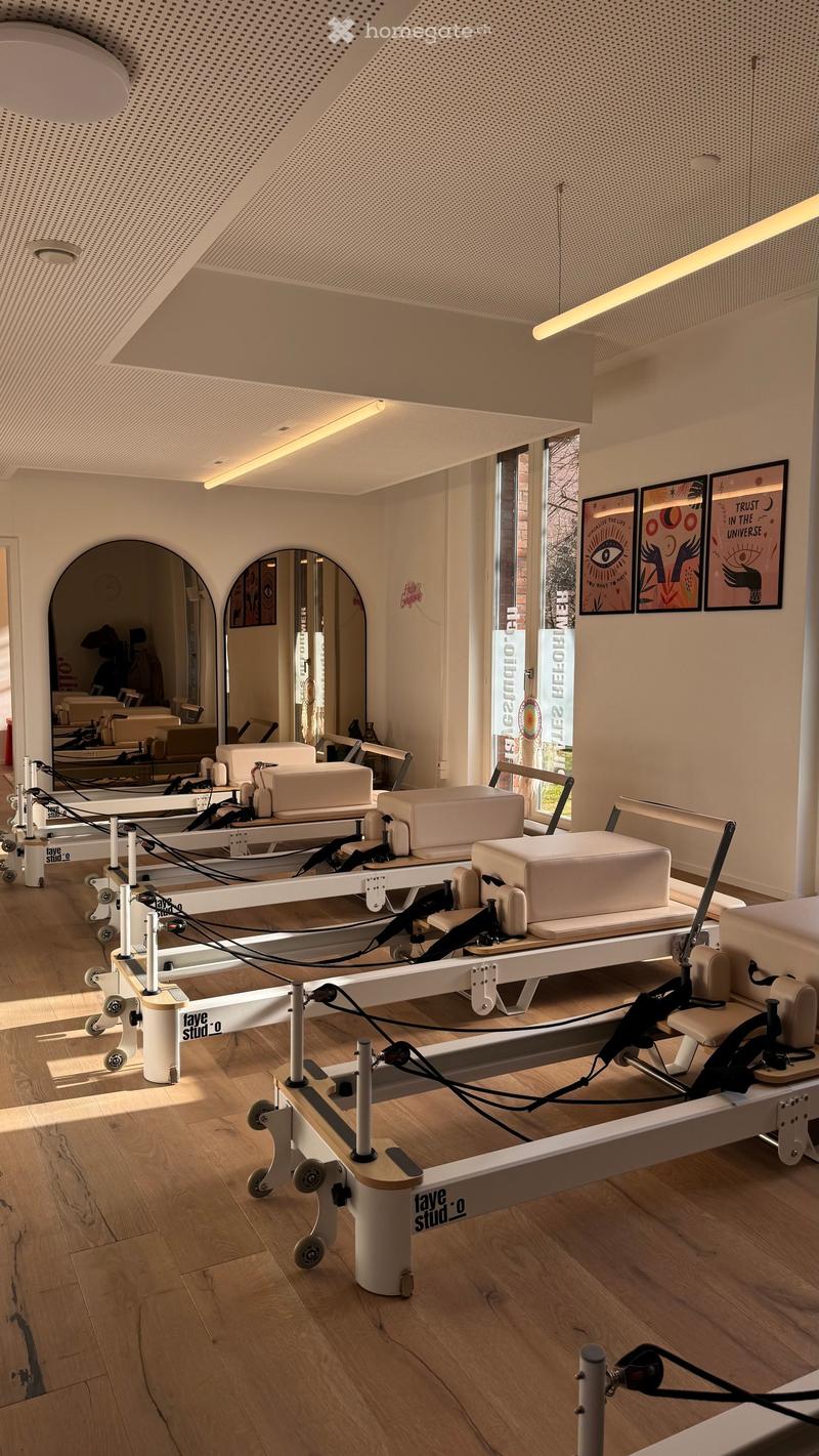 Modern fitness studio with wooden flooring, large mirrors, exercise machines, and artwork on the walls.