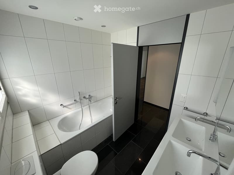 Modern bathroom with white tiled walls, a bathtub, double sink, toilet, and built-in cabinets.