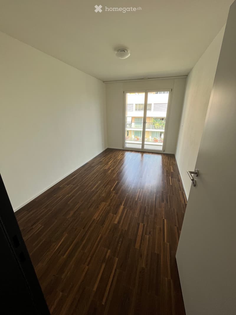 Empty room with wooden flooring, white walls, and a sliding glass door leading to a balcony.