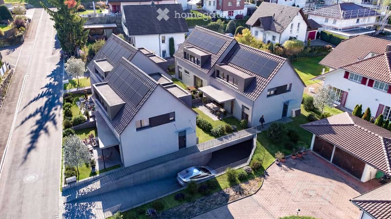 Aerial view of a residential neighborhood with multiple houses, solar panels on roofs, well-maintained gardens, and a parked car in a driveway.