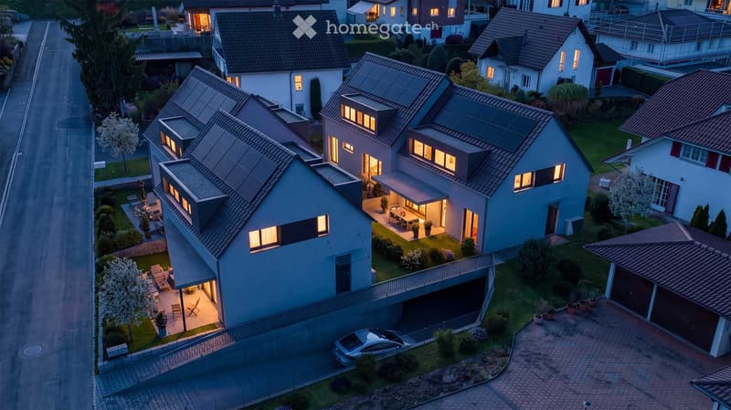 Aerial view of a residential neighborhood with modern houses, solar panels, well-maintained gardens, and parked cars.