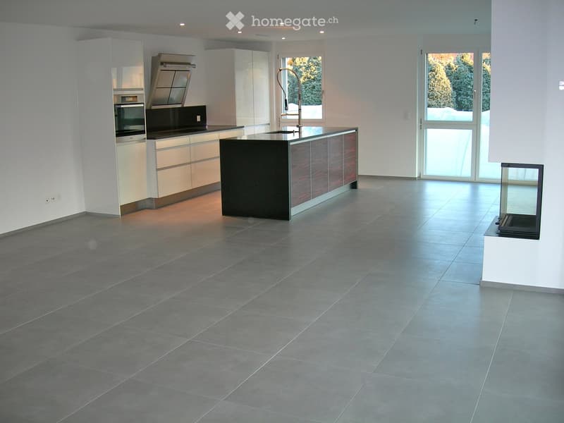 Modern kitchen with a central island, built-in oven, sleek cabinets, and a large window overlooking a snowy landscape.